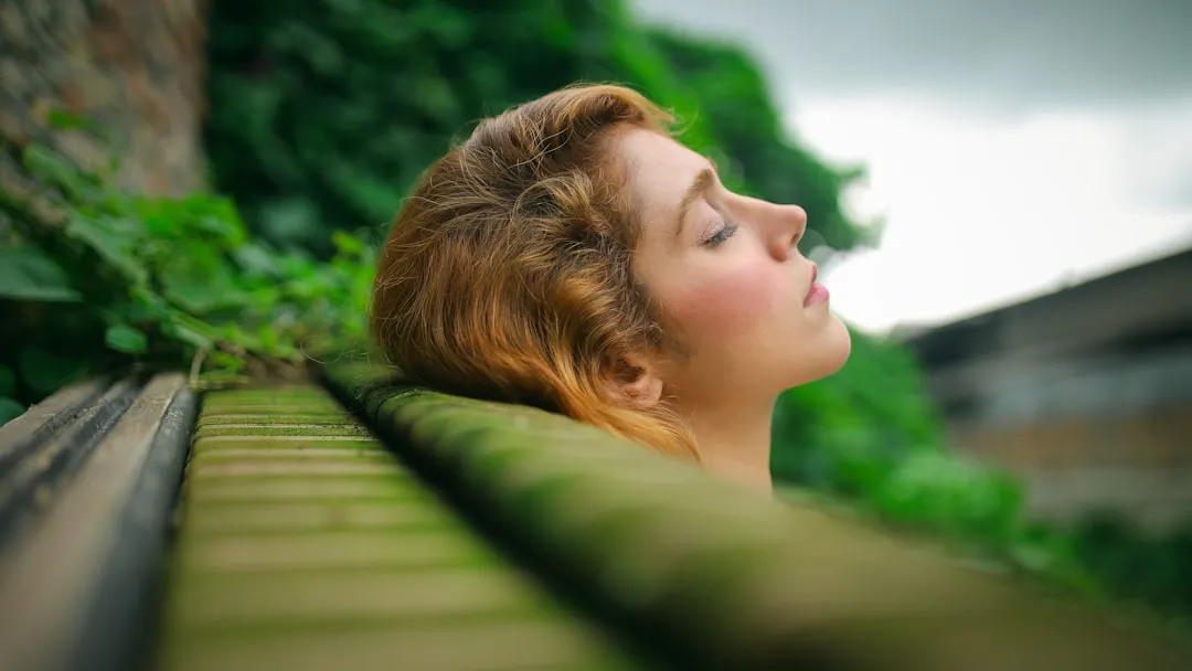 Rêveuse relaxant avec la tête reposant sur un banc en bois, entourée de verdure luxuriante dans un espace naturel apaisant, symbolisant le bien-être et la méditation.